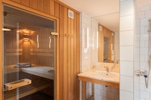 Ein Badezimmer mit Holzwandverkleidung, einer Glaskonstruktion für die Sauna, einem Waschbecken und einem Spiegel.