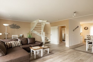 Ein Wohnzimmer mit braunem Ledersofa, einer weißen Treppe und einem Essbereich mit Tisch und Stühlen.