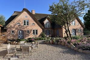 A brick house with a thatched roof, a gravel patio, and outdoor seating. - "Reethus" in the house on the dike (Vollerwiek)