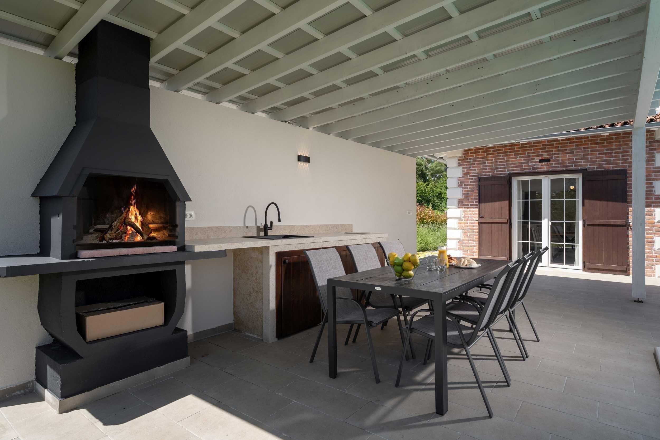 An outdoor kitchen with a built-in grill, dining table, and chairs.