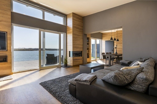 Ein modernes Wohnzimmer mit großem Fenster, Kamin, einer Couch und einem Essbereich.