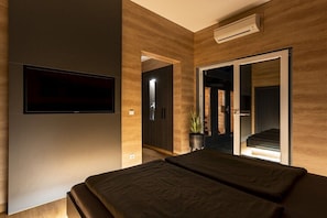 Ein modernes Schlafzimmer mit einem Bett, einem an der Wand befestigten Fernseher und einer Schiebetür, die auf einen Balkon führt.