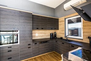Eine moderne Küche mit dunklen Holzschränken, einem eingebauten Backofen, einer Kaffeemaschine und einem Fenster mit Jalousien.