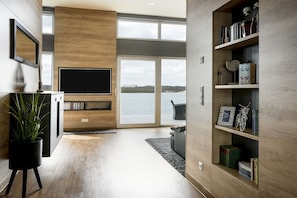 Ein modernes Wohnzimmer mit großem Fernseher, Holzregalen und Blick auf das Wasser.