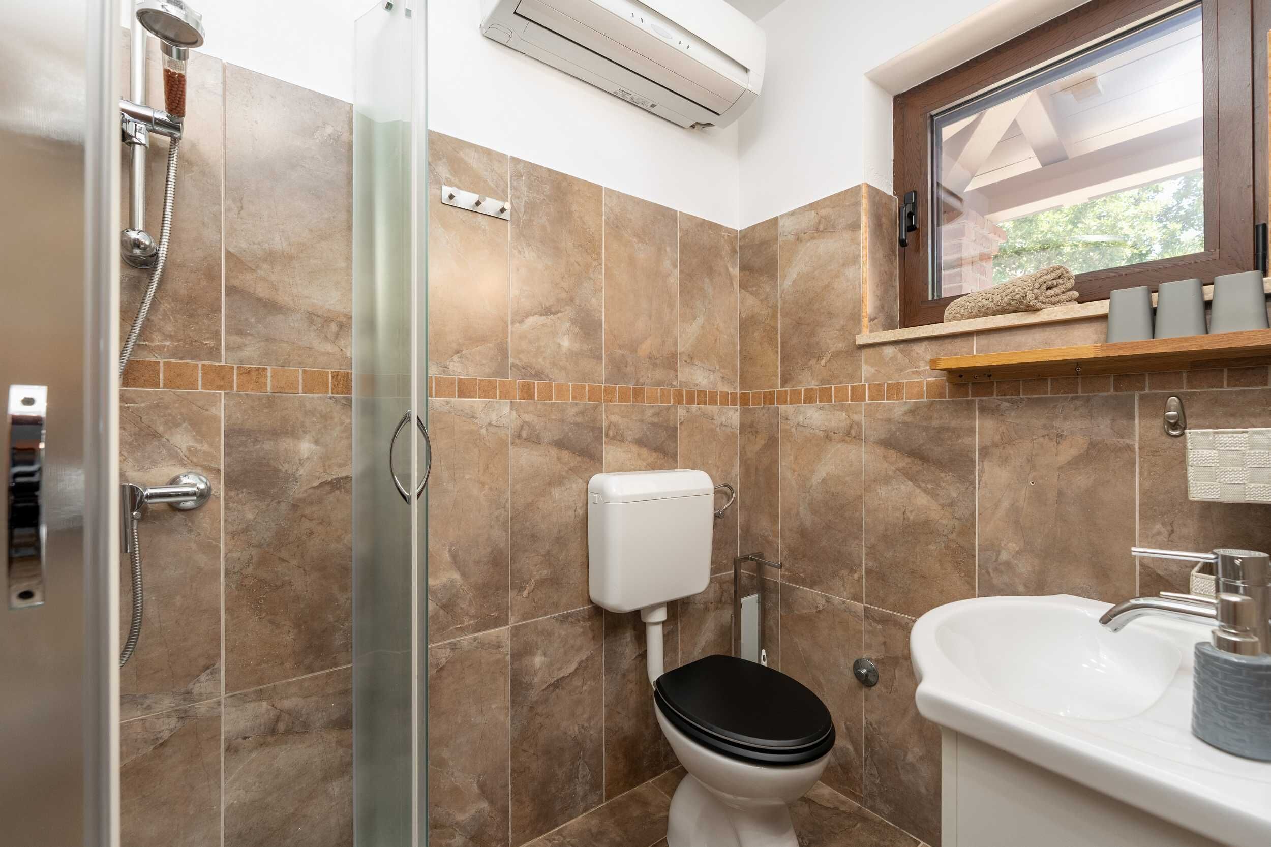 A bathroom with a shower, toilet, sink, and a window with a towel rack.