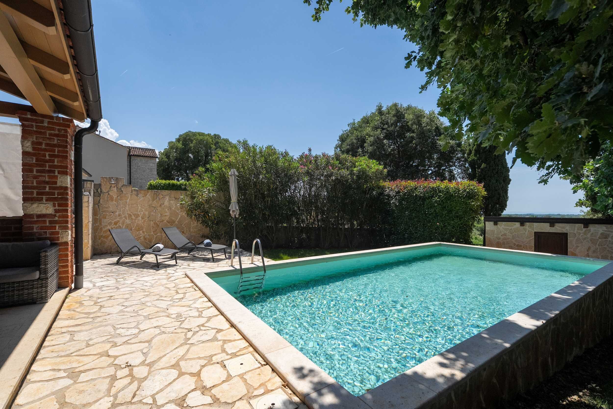 A rectangular swimming pool with a stone deck, two lounge chairs, and a stone wall.
