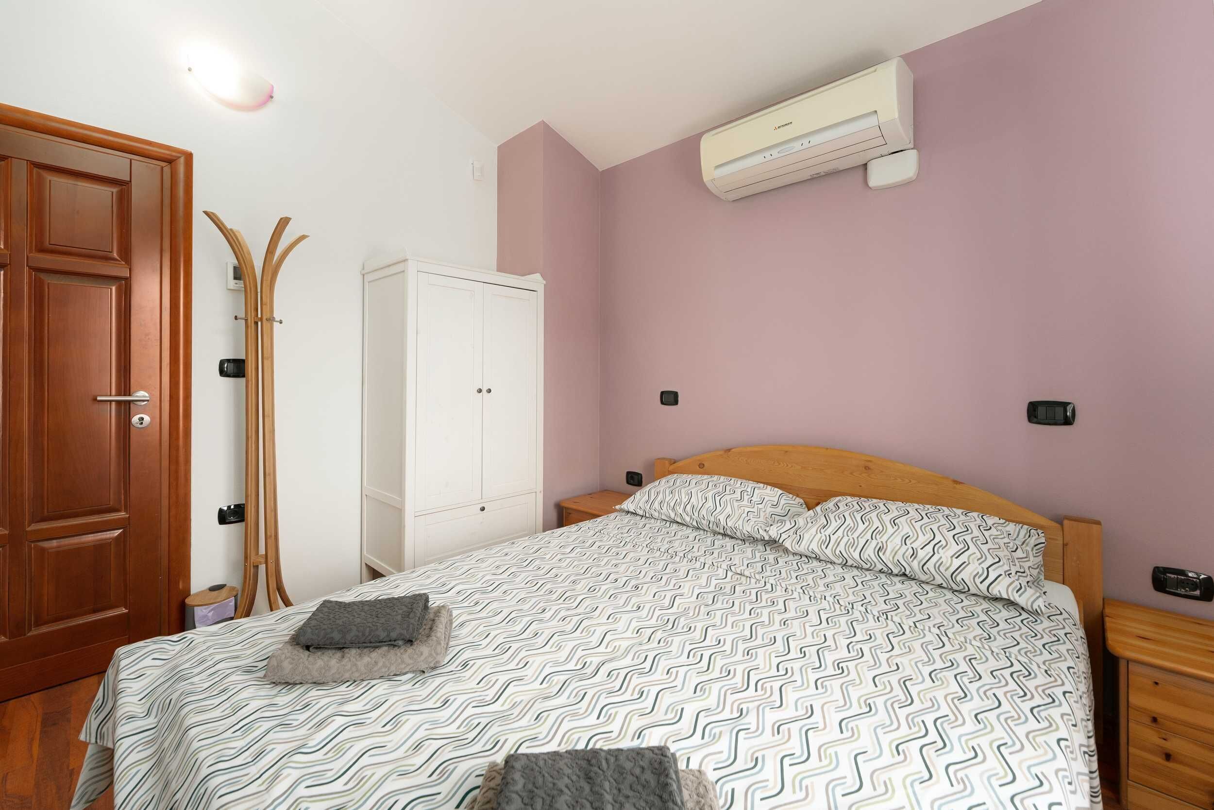 A bedroom with a bed, wooden wardrobe, and an air conditioning unit.
