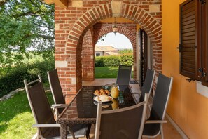 Ein Ziegelbogen führt zu einer Terrasse mit einem für zwei Personen gedecktem Tisch, umgeben von Stühlen.