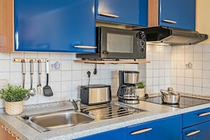 Eine Küche mit blauen Schränken, einer Spüle aus Edelstahl, einer Mikrowelle, einem Toaster und einer Kaffeemaschine.
