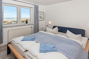 Ein Schlafzimmer mit Bett, Fenster mit Meerblick, Heizkörper und einer Wandlampe.