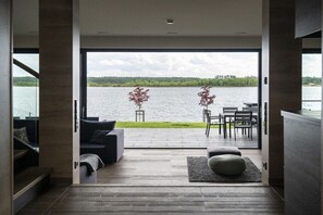 Ein modernes Interieur mit einer großen Schiebeglasdoor, die auf eine Terrasse mit Blick auf ein Gewässer führt.