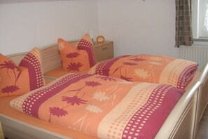 A bed with floral-patterned bedding, a bedside table with a clock, and a window with curtains. - Holiday apartment with 2 bedrooms (Gelenau)