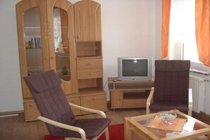 Ein Wohnzimmer mit zwei Sesseln, einem Fernseher und einer Holzkommode mit Regalen.