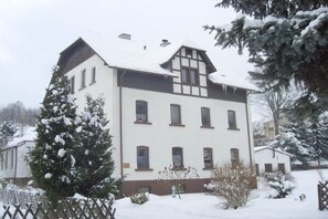 A multi-story building with a symmetrical facade, multiple windows, and a snow-covered roof. - Holiday apartment with 2 bedrooms (Gelenau)
