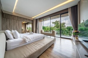 Ein modernes Schlafzimmer mit einem großen Bett, einer Sitzecke und Blick auf Grünflächen.