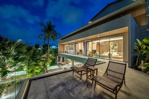 Ein modernes Haus mit Glasbalkon, Sitzgelegenheit im Freien und einem Pool.