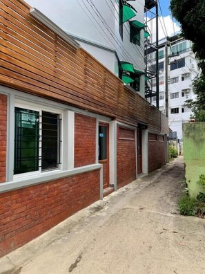 A narrow alleyway with a building featuring a brick facade and wooden slats on the upper part.