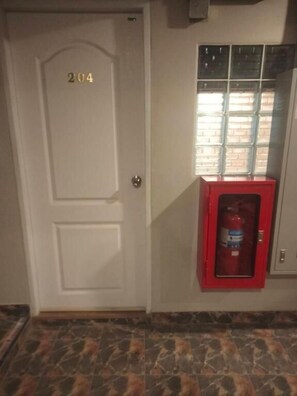 A white door with the number 204, a red fire extinguisher mounted on the wall, and a window with a view of a brick building. - Banhor Residence (AMPHOE MUEANG CHIANG MAI)