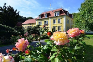 Ein gelbes Gebäude mit rotem Dach, umgeben von üppiger Vegetation und blühenden Rosen.