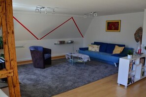 Ein Wohnzimmer mit einem blauen Sofa, einem kleinen Tisch, einer Bücherwand und einem roten, geometrischen Wandmuster.