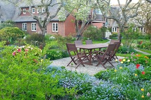A garden with a wooden table and chairs, surrounded by various plants and flowers. - Holiday apartment with 1 bedroom (Oldsum)