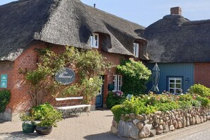 A traditional building with a thatched roof, a sign reading 'Der Bräuhaus,' and a stone wall with plants. - Holiday apartment with 1 bedroom (Oldsum)