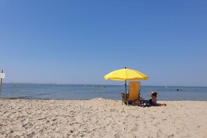 A beach with a yellow umbrella, a chair, and a person sitting. - Holiday apartment with 1 bedroom (Oldsum)