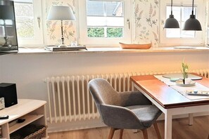A modern kitchen with a dining table, a chair, a radiator, and a window with a view. - Holiday apartment with 1 bedroom (Oldsum)
