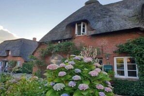 A traditional thatched-roof cottage with a brick exterior, a visible window, and a sign indicating a restaurant. - Holiday apartment with 1 bedroom (Oldsum)