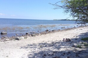 A beach with a rocky shoreline, clear water, and a distant landmass. - Nieby Three-Sided Farmstead - Above the Twete (Steinbergkirche)