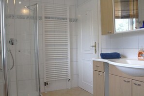 Une salle de bain avec une douche à parois de verre, un porte-serviettes, un lavabo avec un miroir et des toilettes.
