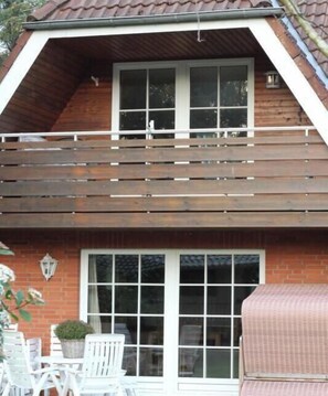 Ein zweistöckiges Haus mit Balkon, großem Fenster und Terrasse mit Gartenmöbeln.