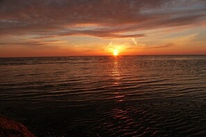 Un coucher de soleil sur une mer calme, avec une côte rocheuse.