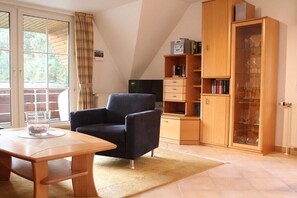 Ein Zimmer mit einem Holztisch, einem schwarzen Sessel, einem Bücherregal und einem Schrank mit Gläsern.