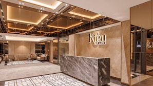 A modern hotel lobby with a reception desk, seating area, and a patterned floor. - Luminous - Kieu by KITA Luxury Apartment (Ho Chi Minh City)