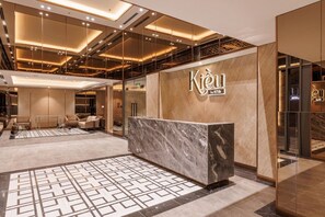 Een moderne hotel lobby met een receptiebalie, zithoek en een vloer met patroon.
