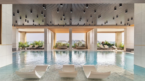 An indoor swimming pool with clear water, surrounded by lounge chairs and potted plants. - Luminous - Kieu by KITA Luxury Apartment (Ho Chi Minh City)