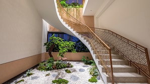 A modern staircase with a geometric railing, surrounded by indoor plants and a pebble-patterned floor. - Luminous - Kieu by KITA Luxury Apartment (Ho Chi Minh City)