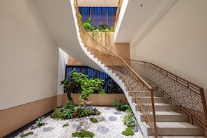 A modern staircase with a geometric railing, surrounded by indoor plants and a pebble-patterned floor. - Luminous - Kieu by KITA Luxury Apartment (Cho Quan)