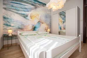 Ein Schlafzimmer mit Bett, Nachttischen, einem Spiegel und einer Wand mit einem farbenfrohen abstrakten Gemälde.