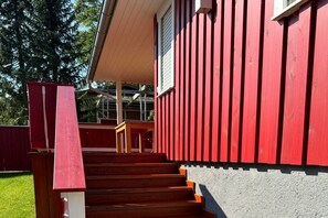 A set of wooden stairs leading up to a house with a red exterior and a white window. - Bungalow with 1 bedroom (Schwielochsee \/OT Jessern)