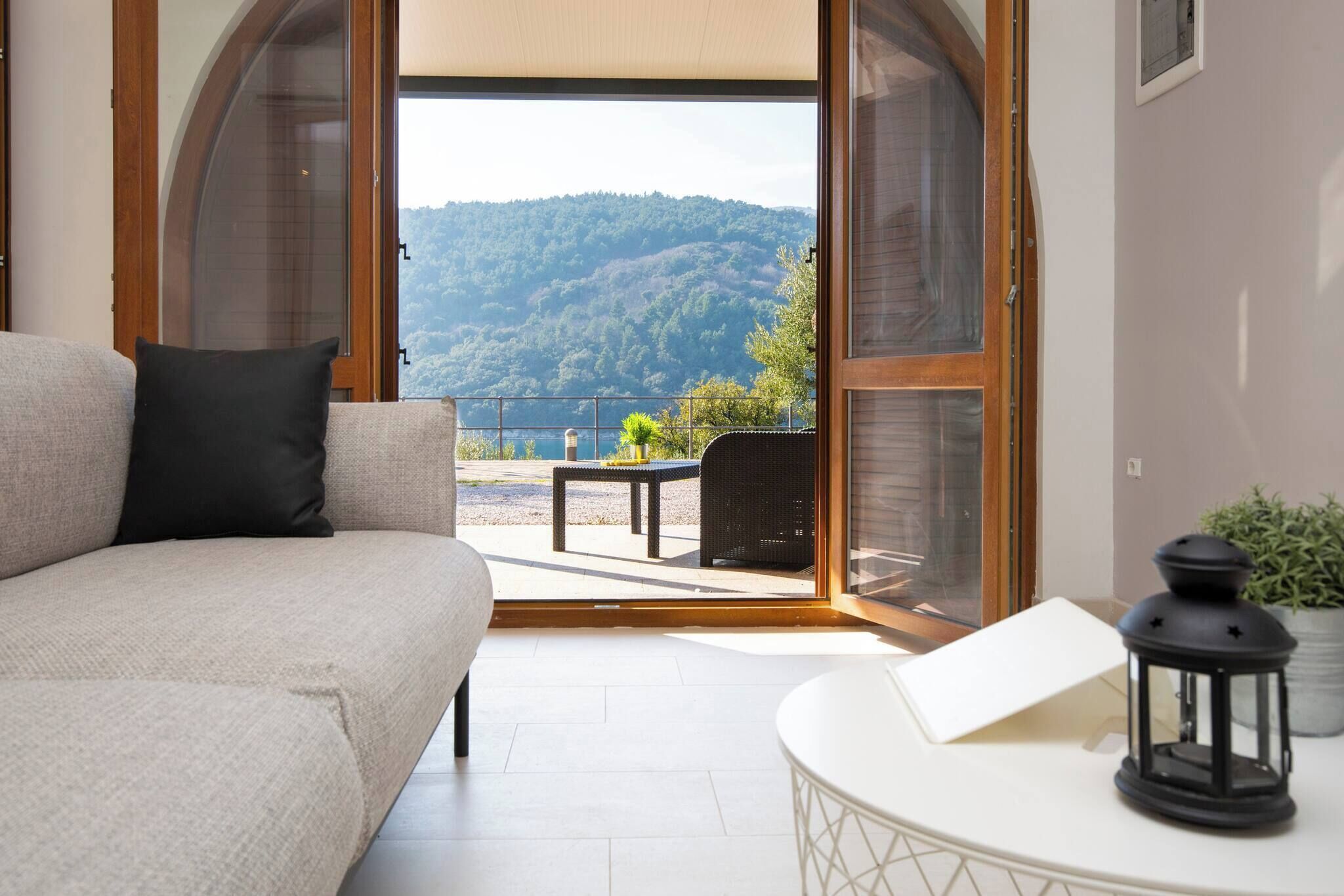 Quarto com sofá, mesa com lanterna e vista para uma paisagem montanhosa através de portas abertas.