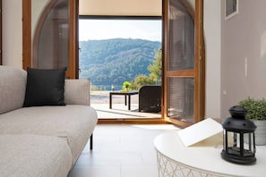Ein Zimmer mit einer Couch, einem Tisch mit einer Laterne und Blick auf eine gebirgige Landschaft durch offene Türen.