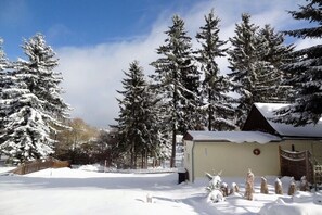 Paisaje nevado con árboles de hoja perenne y un pequeño edificio con techo.