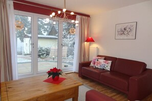 Una sala de estar con un sofá rojo, una mesa de centro de madera, una lámpara roja y una ventana con cortinas.