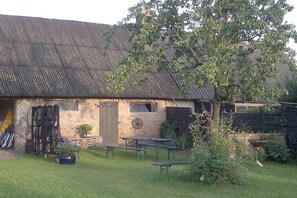 Ein rustikaler Schuppen mit geneigtem Dach, einer Backsteinschmalseite und einer Holztür. Auf dem Gelände befinden sich Picknicktische und ein Blumentopf.