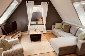 Ein gemütliches Schlafzimmer im Loft-Stil mit großem Fenster, einem Flachbildfernseher, einer Couch und einem kleinen Tisch.