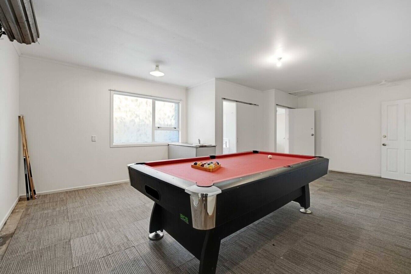 A pool table in a room with white walls, a window, and a door.