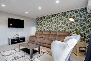 A living room with a sofa, a coffee table, a TV, and a patterned wallpaper.