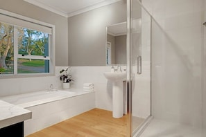 A modern bathroom with a large bathtub, a sink, and a glass-enclosed shower. - Pokeno Country Retreat | Spa, BBQ and Rural Views (Pōkeno)